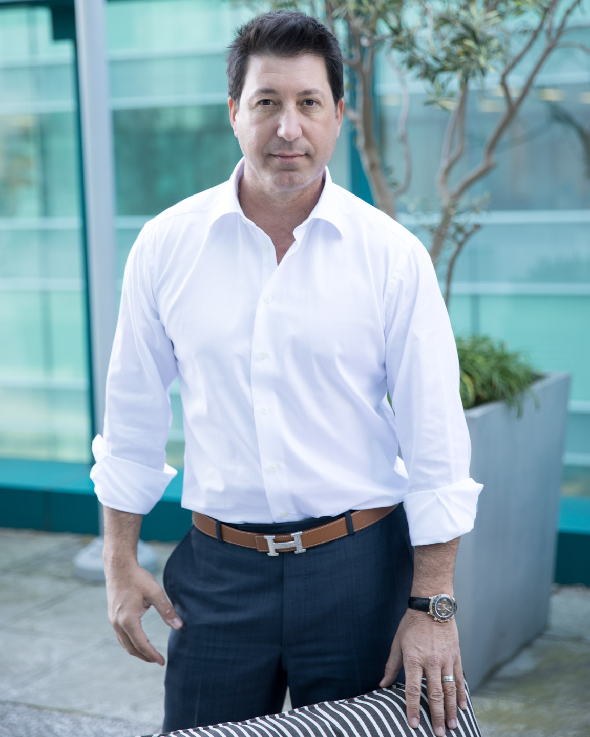 Professional headshot of man in white shirt against modern glass building