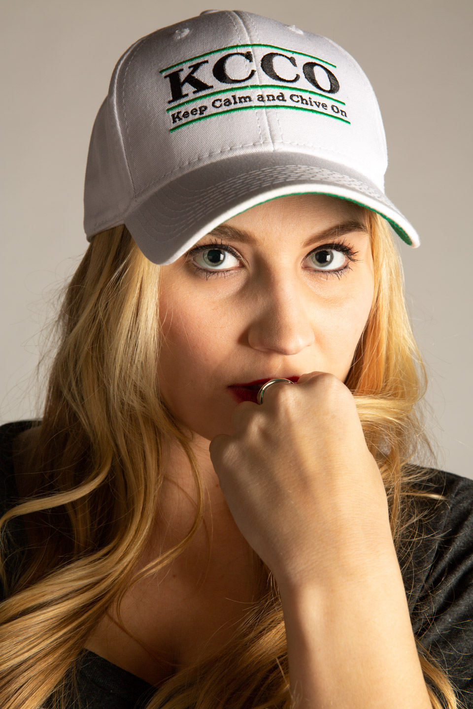 Woman wearing white KCCO cap, thoughtful expression, studio portrait